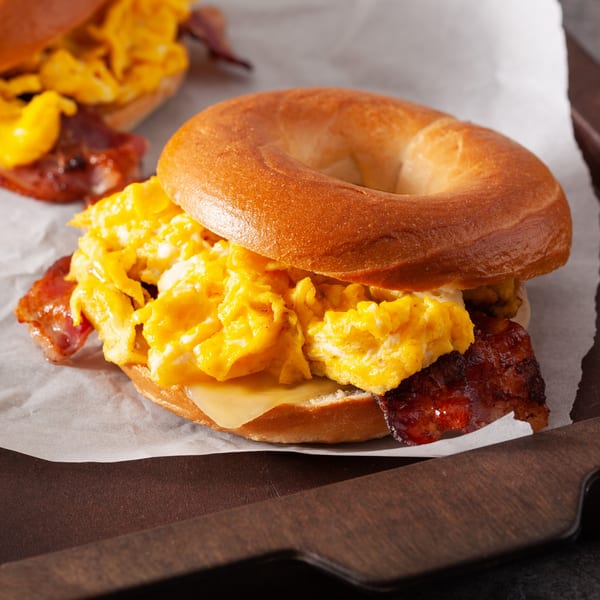 A Sunset Diner breakfast bagel with scrambled eggs, crispy bacon, and melted cheese on parchment paper.