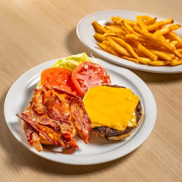 A bacon cheeseburger with lettuce and tomato, alongside a plate of golden french fries.