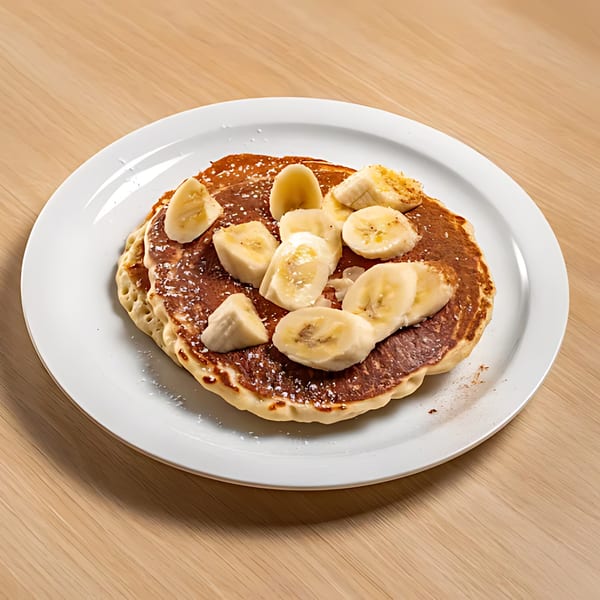 Fluffy pancakes topped with sliced bananas and powdered sugar on a white plate at Sunset Diner.
