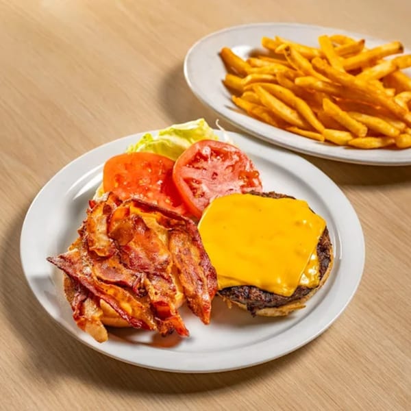 A Sunset Diner bacon cheeseburger with lettuce and tomato, served with a side of golden fries.