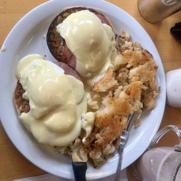 Eggs Benedict with hollandaise sauce and a side of crispy hash browns on a white plate.